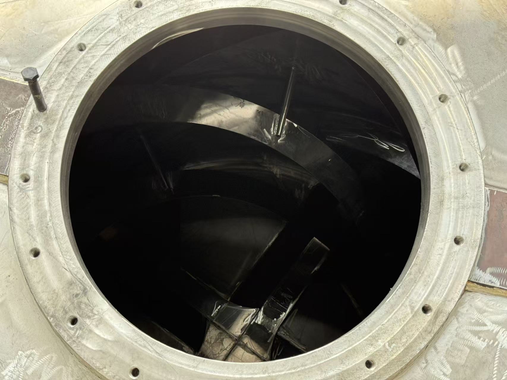 Interior of FBM drum viewed through access manhole, showing polished stainless steel spiral blade assemblies and smooth inner wall surface